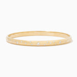 A thin yellow gold bangle bracelet with small, evenly spaced clear gemstones set along the outer band, shown against a plain white background.