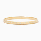 A thin yellow gold bangle bracelet with small, evenly spaced clear gemstones set along the outer band, shown against a plain white background.