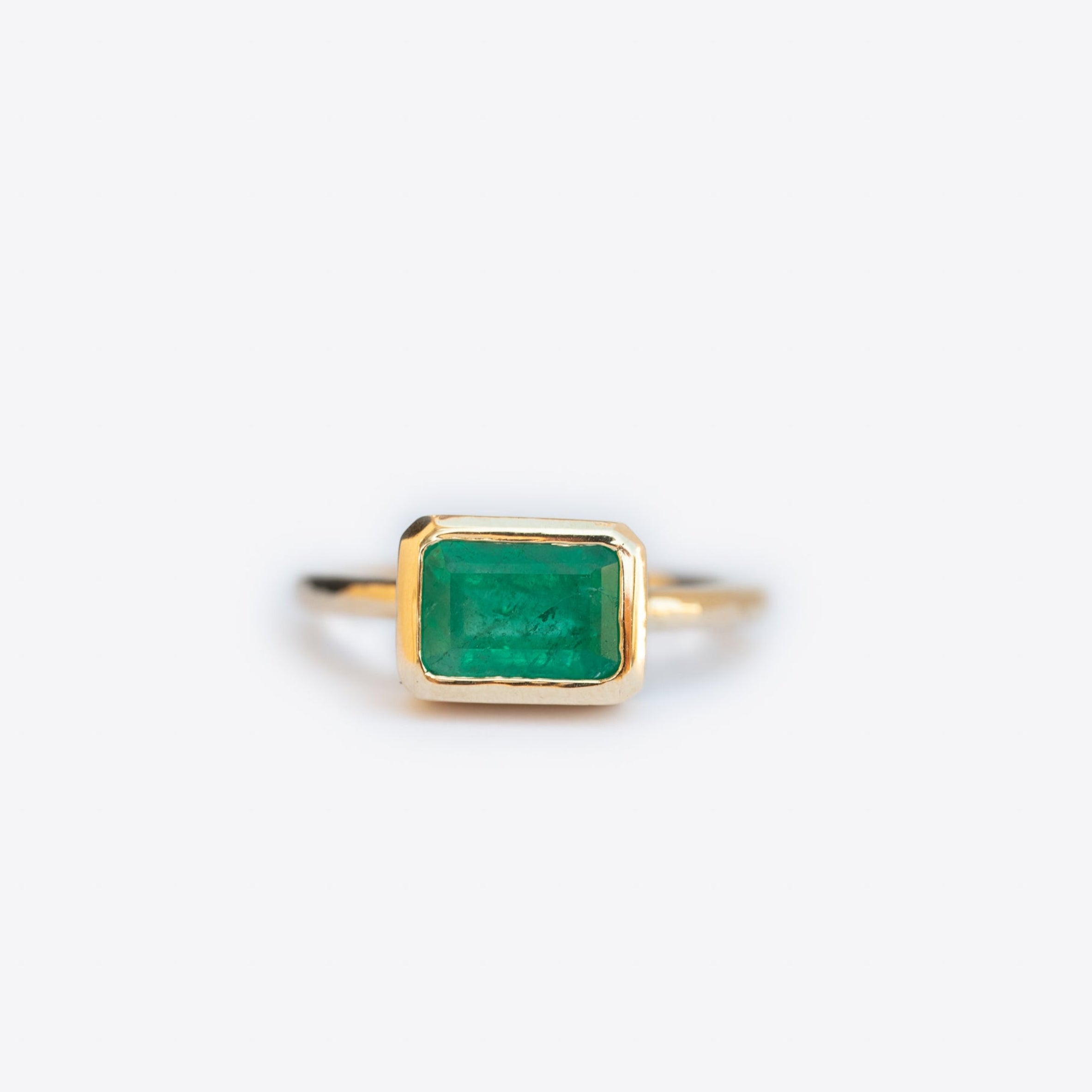 Gold ring with a green emerald on a white background
