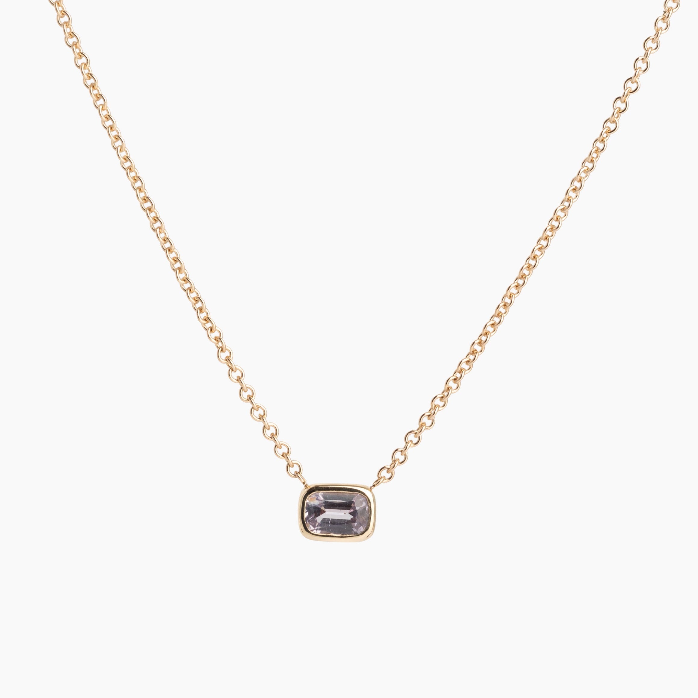 Gold necklace with a rectangular gemstone pendant on a white background