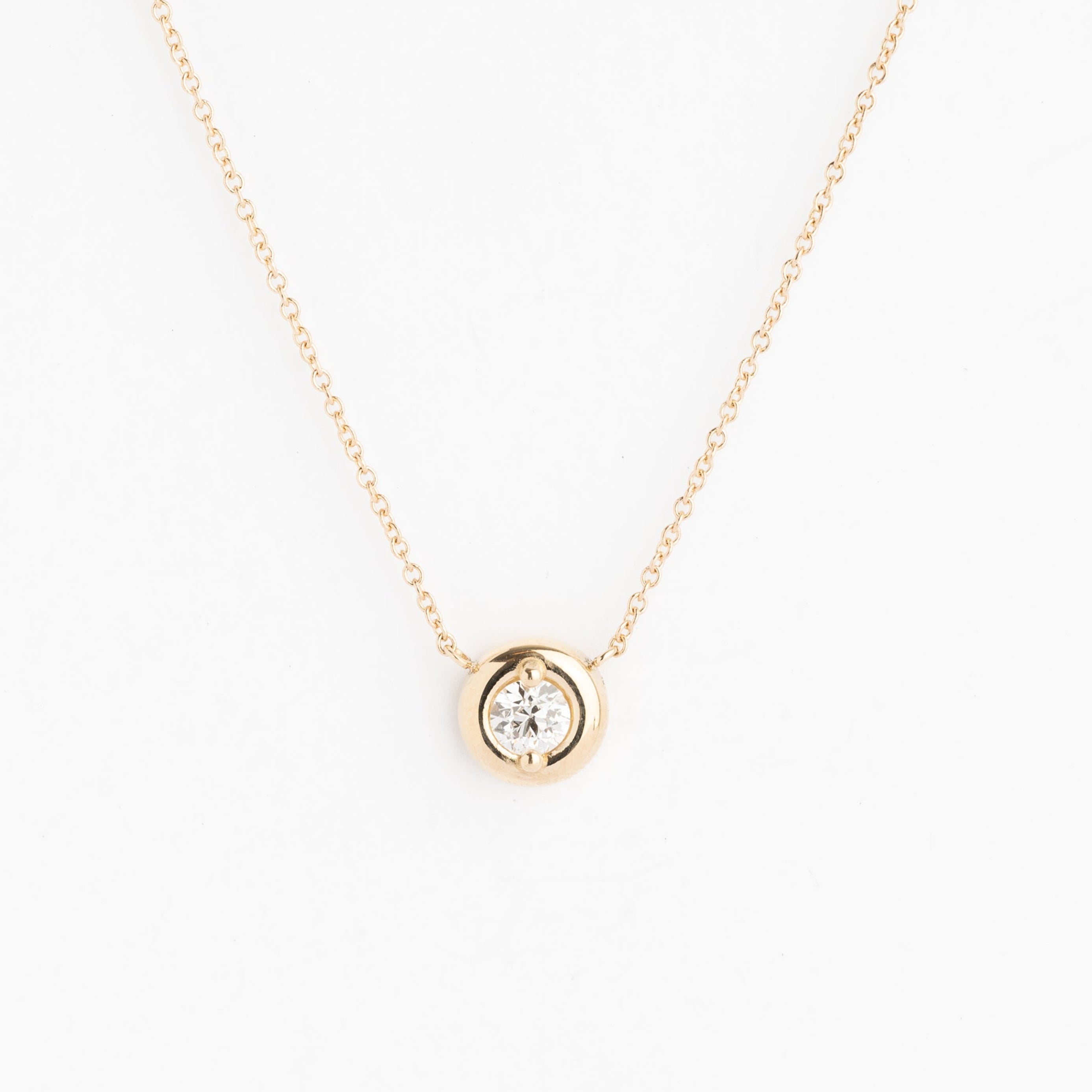 Gold necklace with a small round pendant on a white background